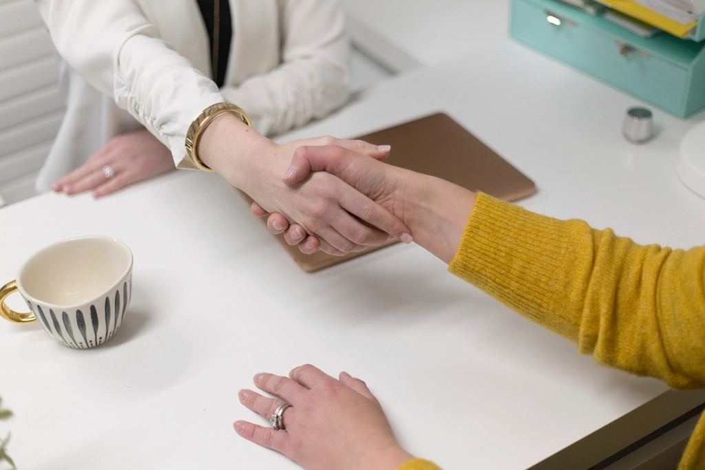 Two people shaking hands over a meeting table